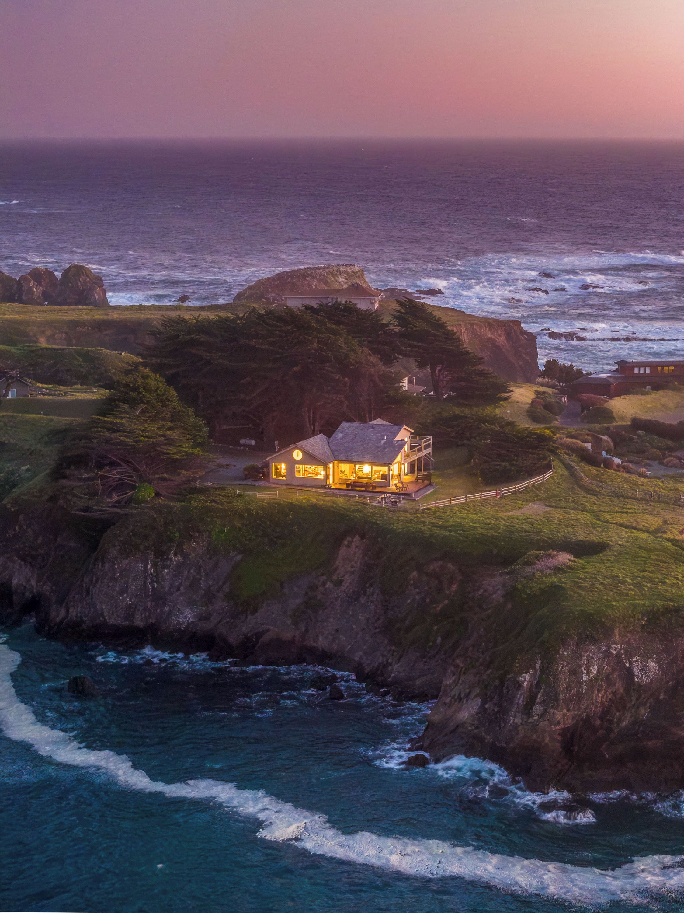 A coastal house with a view of the ocean, surrounded by rocky terrain and greenery.