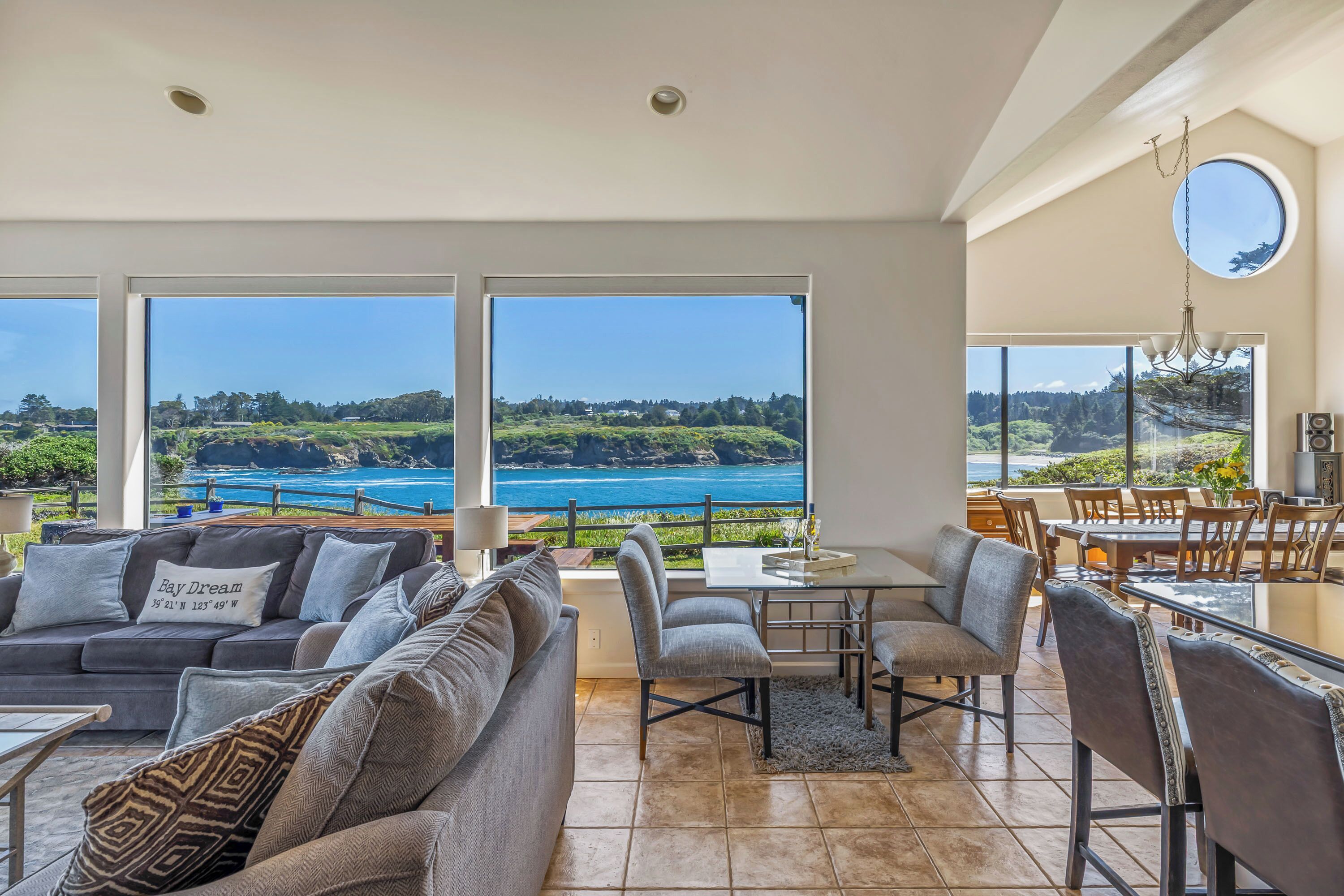 Un vaste espace de vie doté d’une grande fenêtre donnant sur un paysage magnifique, un coin repas avec une table et des chaises, et un coin salon confortable avec un canapé et des coussins.