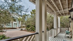 A covered porch with a wooden ceiling and white railings. There is a bench with a cushion and a table with a patterned table runner.