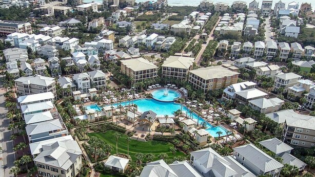 An aerial view of a resort with multiple buildings, a central swimming pool, and surrounding greenery.