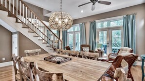 A spacious dining area with a wooden table and chairs, a chandelier, and a staircase.