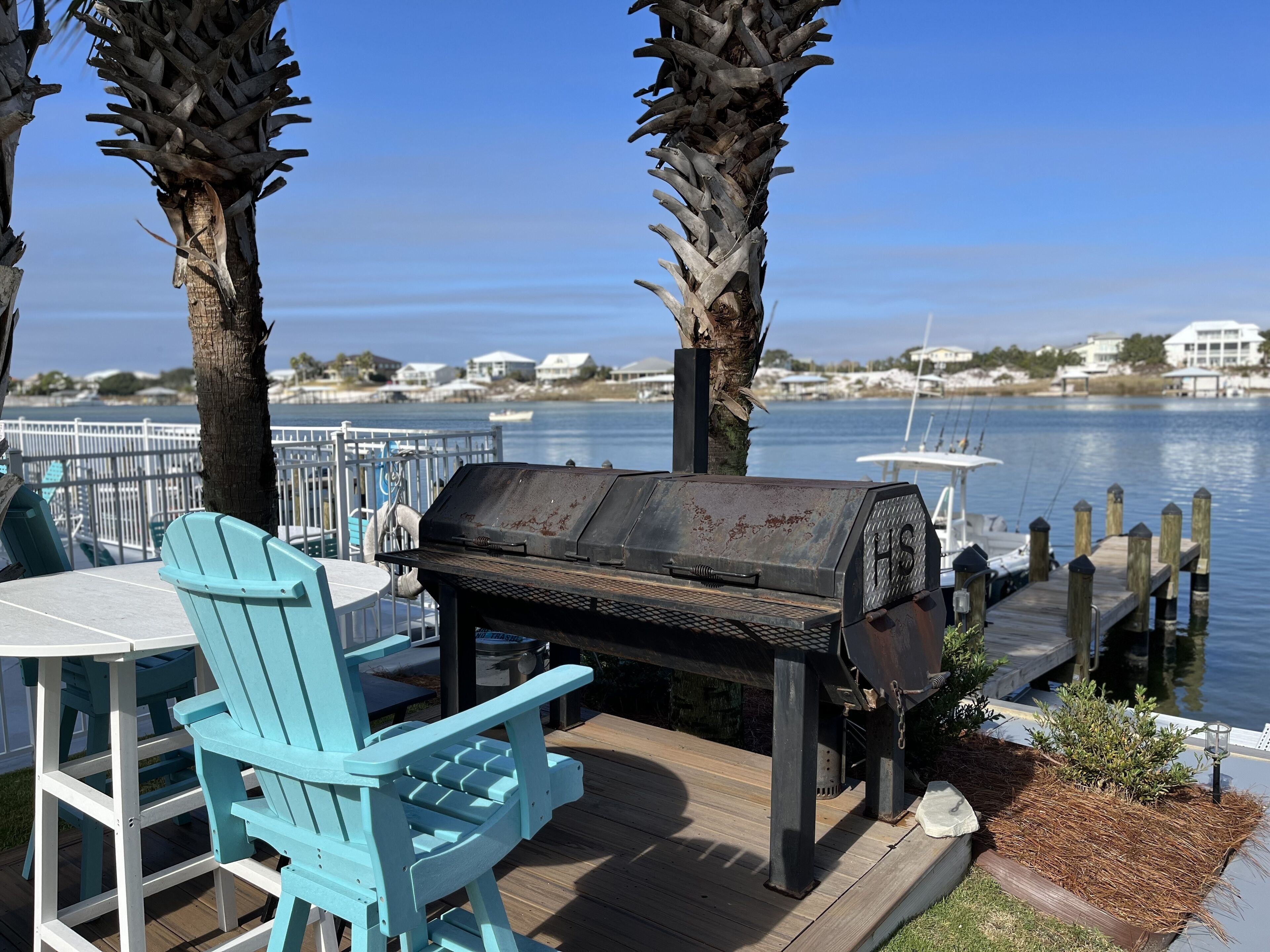 A deck with a grill, turquoise chairs, and a view of the water.