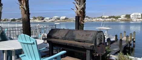 A deck with a grill, turquoise chairs, and a view of the water.