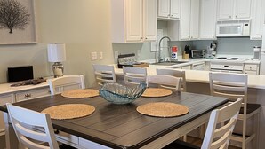 A modern kitchen with white cabinets, a dark wooden dining table, and a central island with a bowl. - Recently updated!  3 bed 3 bath waterfront condo (Orange Beach)