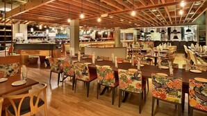 Um restaurante espaçoso com vigas de madeira, mesas com cadeiras florais e um bar ao fundo.
