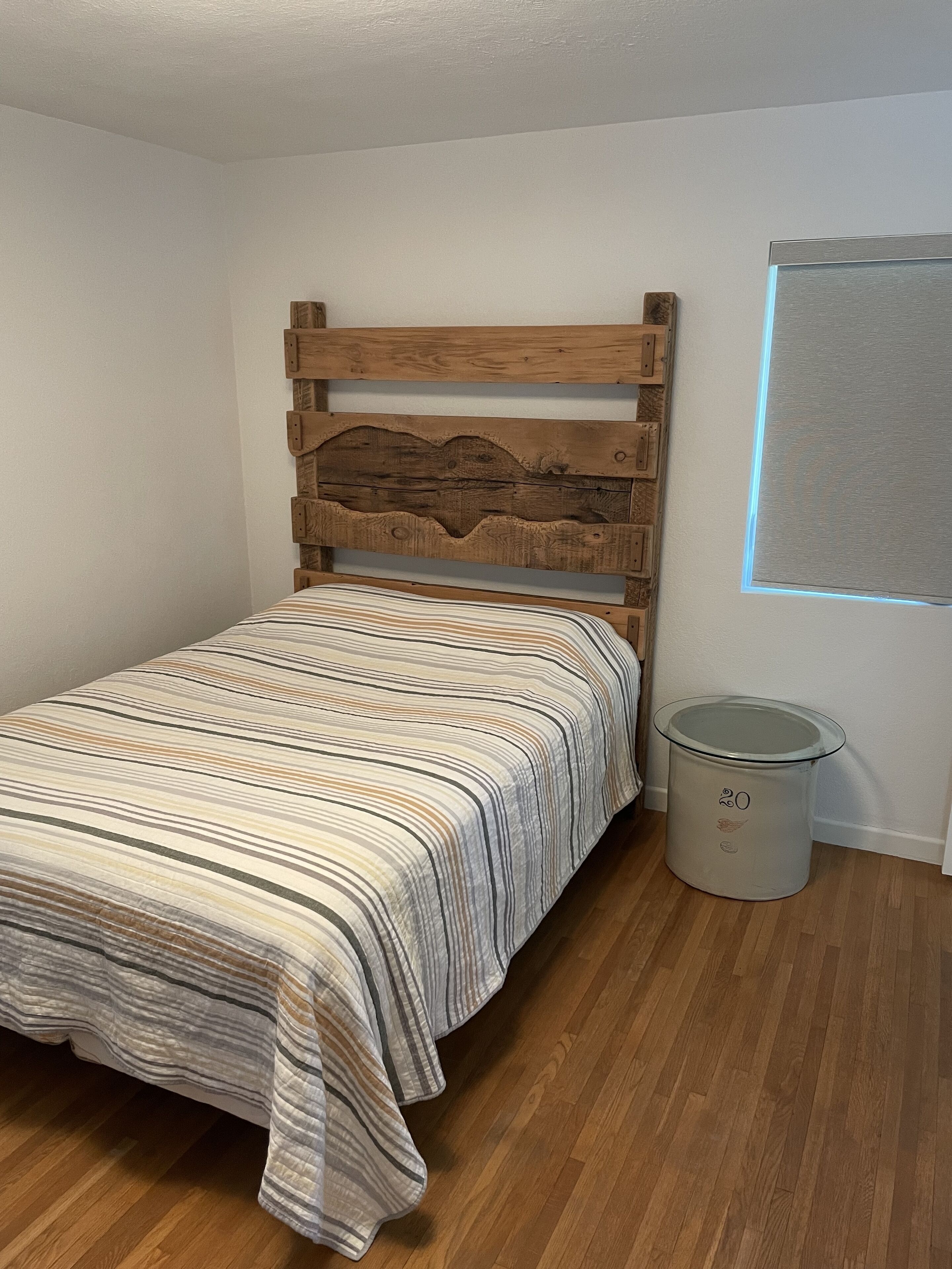 Ein Schlafzimmer mit einem hölzernen Kopfteil, einer gestreiften Bettdecke und einem Mülleimer.