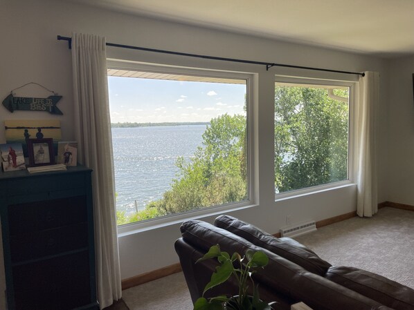 Ein Zimmer mit einem großen Fenster mit Blick auf ein Gewässer, einem braunen Ledersofa und einem blauen Schrank mit gerahmten Bildern.