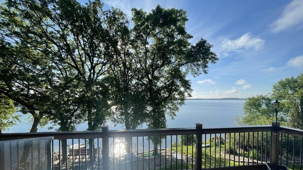 A wooden deck with a railing overlooking a lake, surrounded by trees. - Beautiful home on Clear Lake! Amazing views 🌅 Great fishing 🎣 Great boating 🚤 (Lake City)