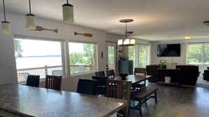A spacious kitchen with granite countertops, wooden chairs, and a dining table. There are large windows offering views of a lake and trees. - Beautiful home on Clear Lake! Amazing views 🌅 Great fishing 🎣 Great boating 🚤 (Lake City)