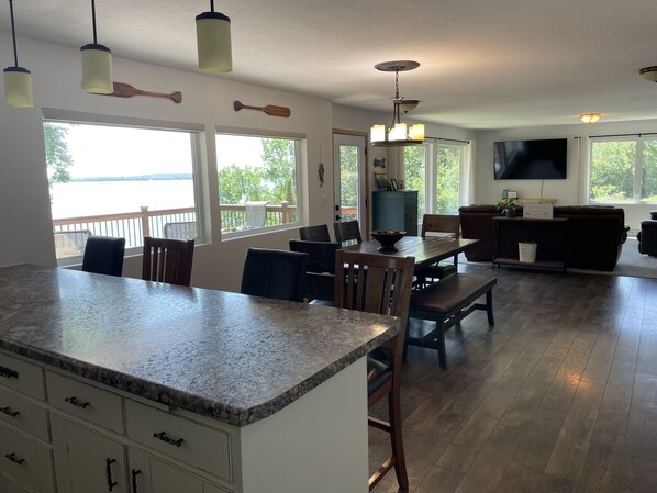 A spacious kitchen with granite countertops, wooden chairs, and a dining table. There are large windows offering views of a lake and trees. - Beautiful home on Clear Lake! Amazing views 🌅 Great fishing 🎣 Great boating 🚤 (Lake City)