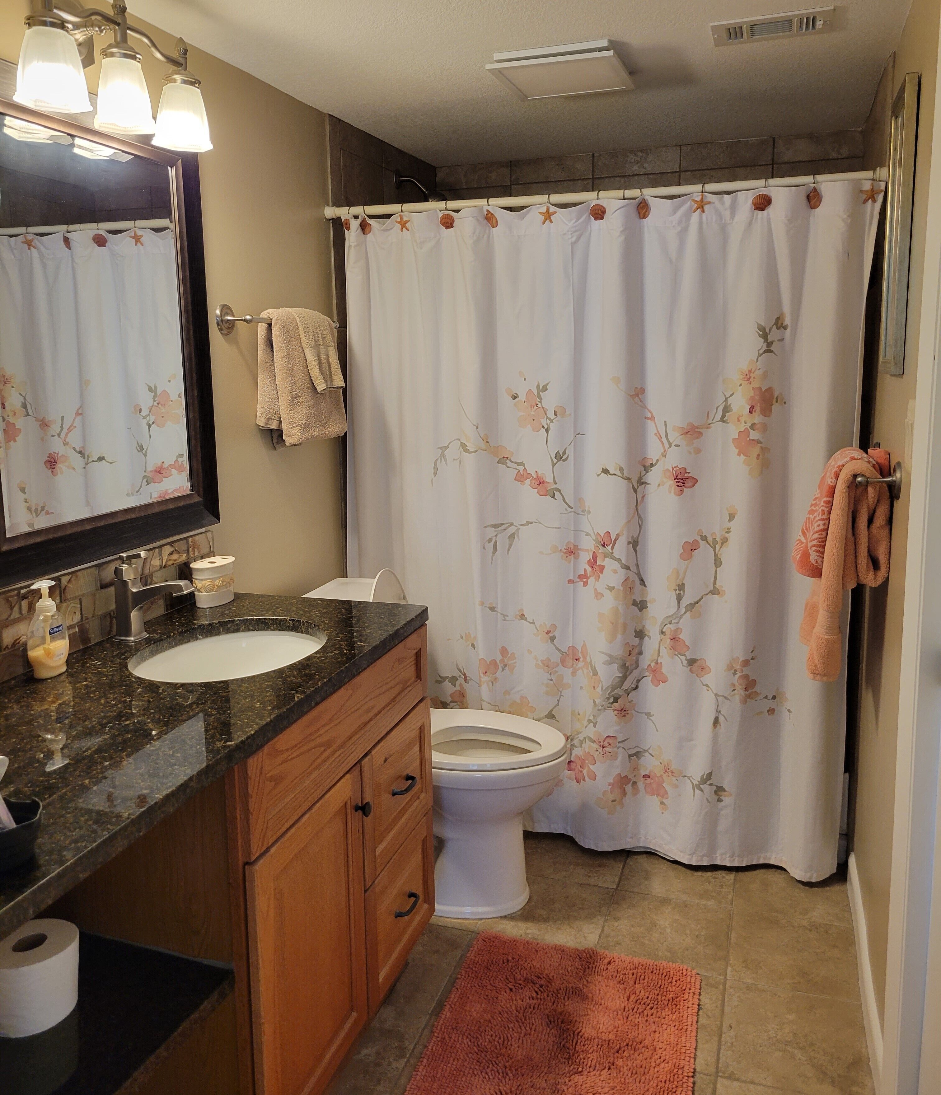 A bathroom with a marble sink, a toilet, a mirror, and a shower curtain with floral patterns.