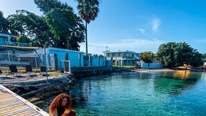 Un muelle de madera que se adentra en aguas azules y transparentes, con dos personas sentadas allí.