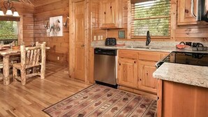 A wooden cabin interior with a dining area, kitchen, and a large window. - Moondance: Pet Friendly - Brand New Hot Tub - Cozy Wooded Atmosphere (Sevierville)