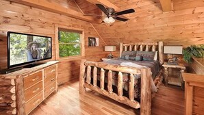 A wooden cabin bedroom with a bed, a television, a ceiling fan, and a window. - Moondance: Pet Friendly - Brand New Hot Tub - Cozy Wooded Atmosphere (Sevierville)