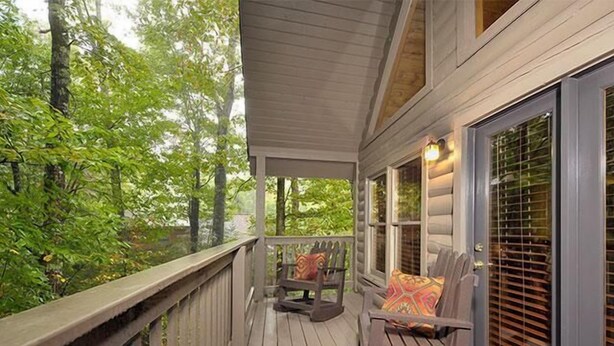 A wooden deck with two rocking chairs and a window with blinds. - Moondance: Pet Friendly - Brand New Hot Tub - Cozy Wooded Atmosphere (Sevierville)