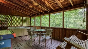 A wooden deck with a pool table, chairs, and a swing.