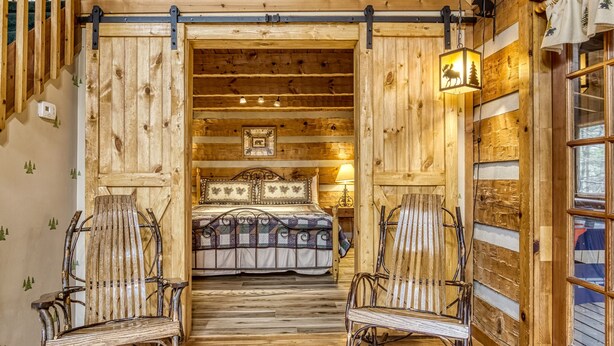 A rustic wooden room with a bed, two rocking chairs, and a wooden floor.