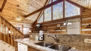 A kitchen with granite countertops, stainless steel sinks, wooden beams, and a large window.