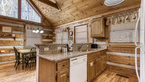 A log cabin-style kitchen with wooden walls, a granite countertop, a dishwasher, and a dining area with a table and chairs.