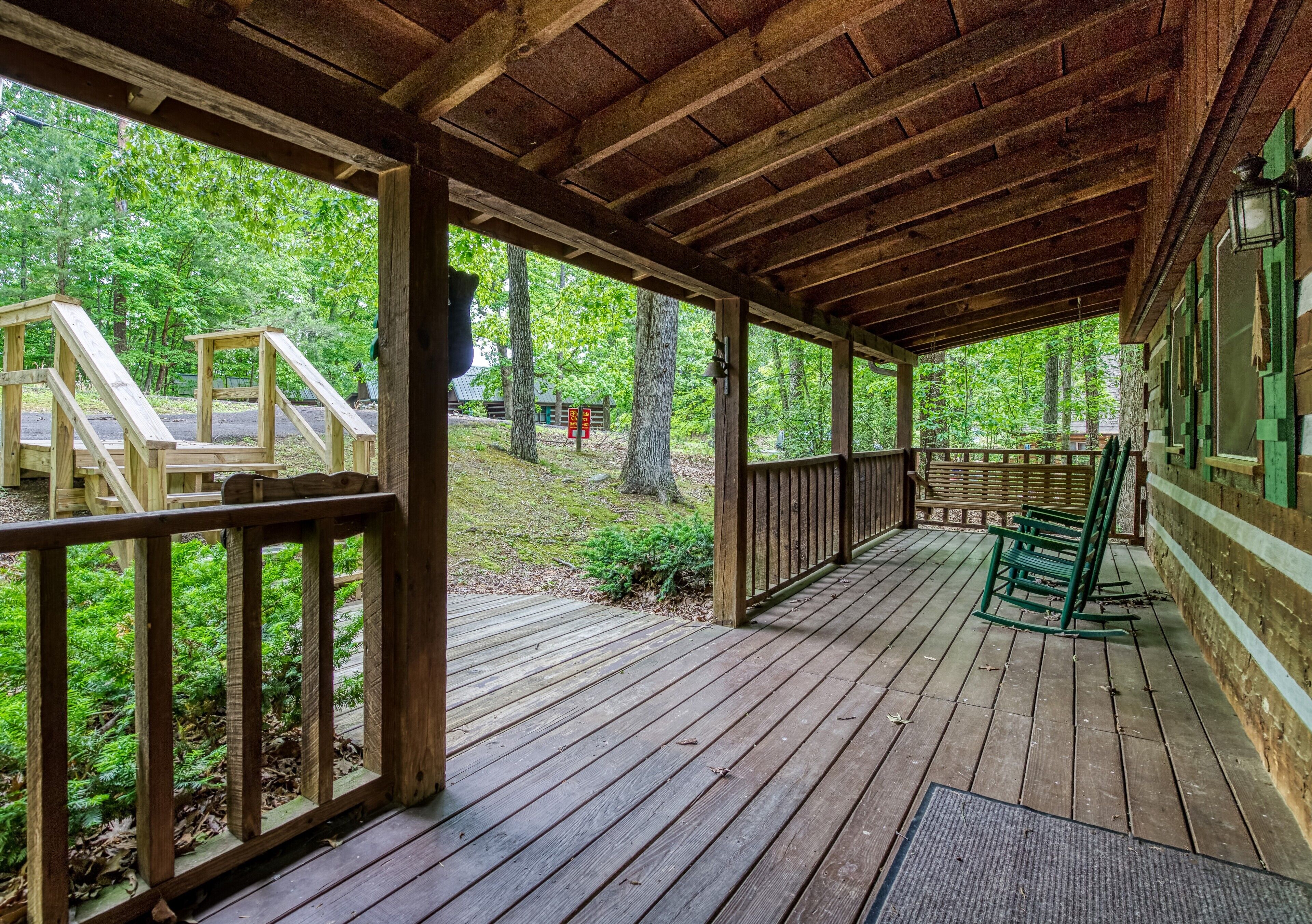 Una terraza de madera con un área cubierta, barandillas de madera y vistas a un bosque.