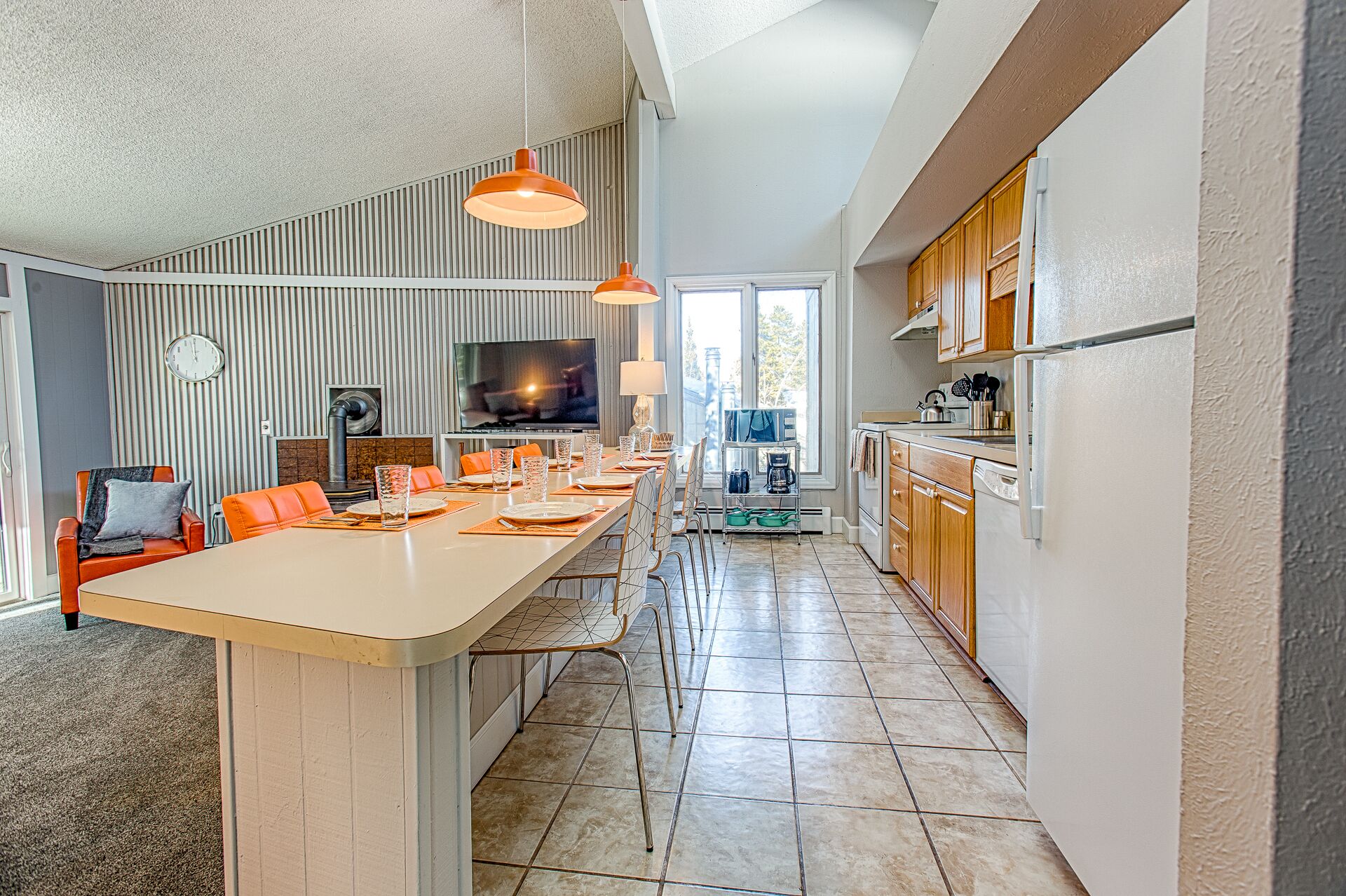 Una cocina moderna con una isla grande, electrodomésticos integrados y un comedor con sillas anaranjadas.