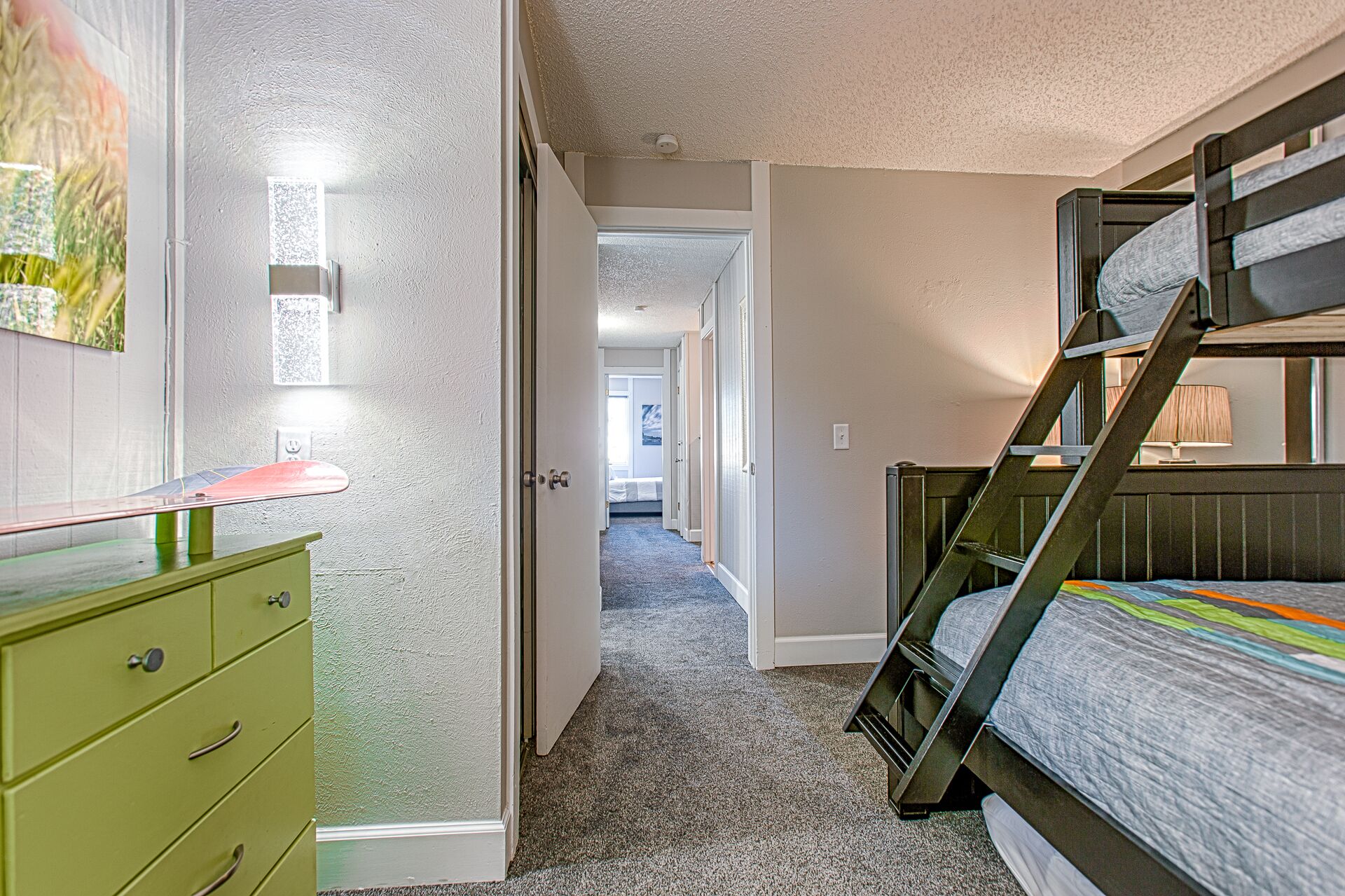 A bedroom with bunk beds, a green dresser, and a hallway leading to another room.