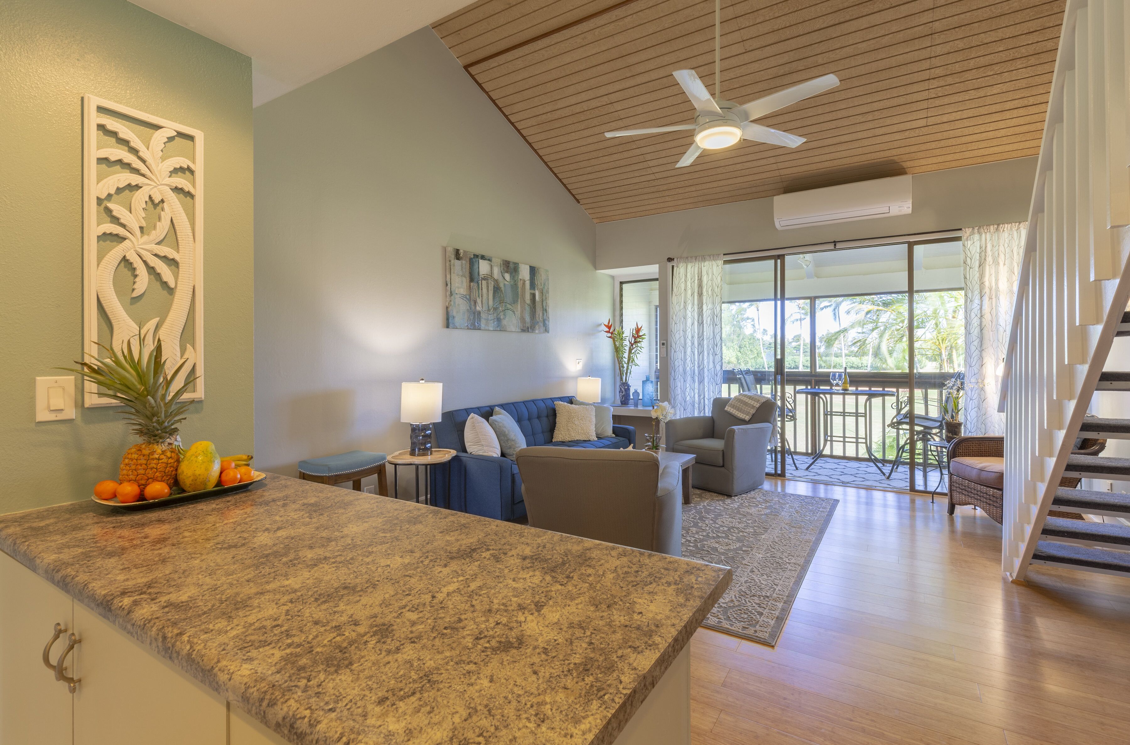 A spacious living area with a kitchen counter, a sofa set, a dining table, and a staircase leading to an upper level.