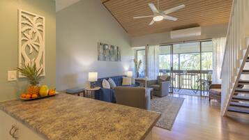 A spacious living area with a kitchen counter, a sofa set, a dining table, and a staircase leading to an upper level.