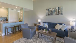 A modern living room with a blue sofa, two armchairs, a coffee table, and a kitchen area with a counter and stools. - Resort Living Off the Beaten Path
AC , WIFI, and Fully Remodeled Bathroom (Kahuku)