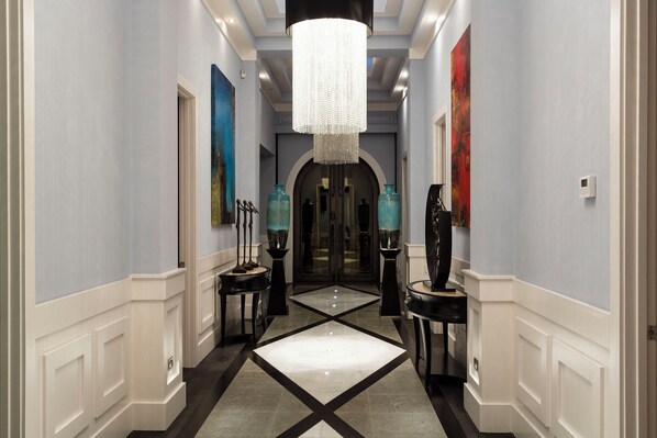 A hallway with a chandelier, artwork, and a tiled floor.