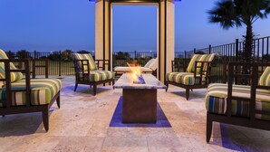 An outdoor seating area with a fire feature, surrounded by chairs with striped cushions, under a covered structure with blue lighting. - Waterfront Home-Bowling Alley, Cinema, Sauna, Outdoor Grilling, Pool w/ Slide  (Four Corners)