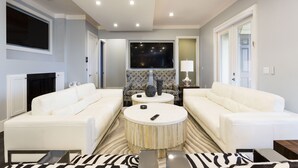 A modern living room with two white sofas, a round coffee table, and a flat-screen TV mounted on the wall. - Waterfront Home-Bowling Alley, Cinema, Sauna, Outdoor Grilling, Pool w/ Slide  (Four Corners)