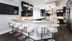 A modern kitchen with a central island, bar stools, stainless steel appliances, and pendant lighting. - Waterfront Home-Bowling Alley, Cinema, Sauna, Outdoor Grilling, Pool w/ Slide  (Four Corners)