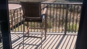 Un balcone con una sedia e un tavolo di legno, una ringhiera in metallo e un tappetino di benvenuto.