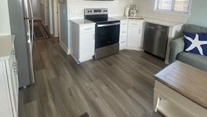 Una cucina moderna con mobili bianchi, forno a microonde, forno e lavastoviglie. Presente un ventilatore a soffitto, una finestra con persiane e un pavimento in legno.