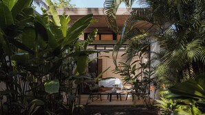 Un edificio moderno con un área de estar al aire libre techada, rodeada de exuberante vegetación tropical.
