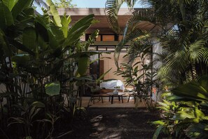 Un bâtiment moderne doté d’un espace extérieur aménagé, abrité et entouré d’une végétation tropicale luxuriante.