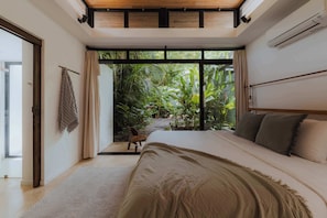 A bedroom with a large bed, a view of greenery outside, and a sliding door leading to an outdoor area.