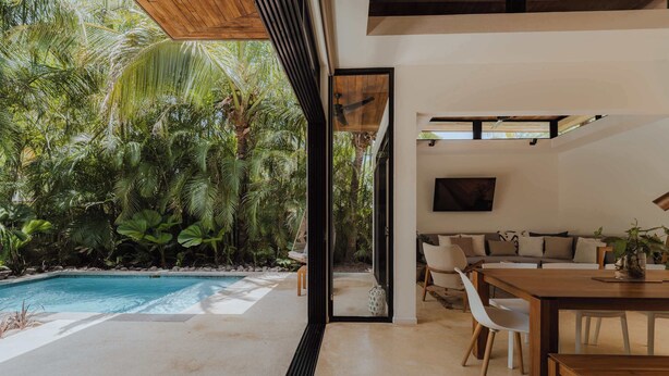 Un interior moderno con piscina, zona de comedor y sala de estar con vistas a la vegetación tropical.