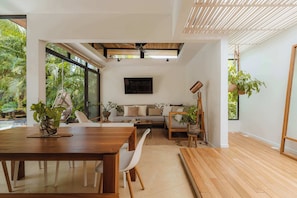 A modern interior with a wooden dining table, white chairs, a sofa, and a ceiling fan.