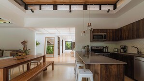 Cocina moderna con una isla de madera, taburetes blancos y una zona de comedor con banco.