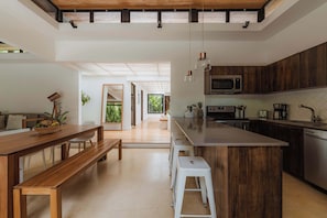 Cocina moderna con una isla de madera, taburetes blancos y una zona de comedor con banco.