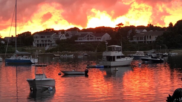 A marina with boats docked, surrounded by houses and trees under a sunset sky.