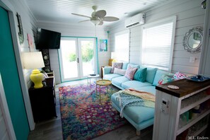 Ein gemütliches Wohnzimmer mit einem türkisfarbenen Sofa, einem farbenfrohen Teppich und einem Deckenventilator.