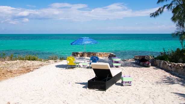 Una playa con una fila de sillas de playa coloridas y un paraguas azul a rayas.