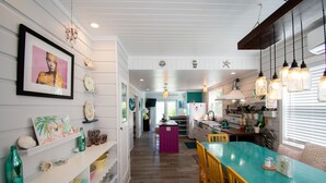 Una cocina con armarios blancos, una mesa de comedor color turquesa y lámparas colgantes.