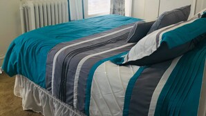 Une chambre à coucher avec un lit, un radiateur, une fenêtre avec des rideaux et une porte.