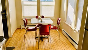 Una habitación con piso de madera, una mesa con cuatro sillas rojas y dos ventanas con persianas.