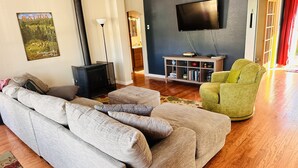 Una sala de estar con un sofá gris, un sillón verde, un televisor de pantalla plana, una estantería y una chimenea.