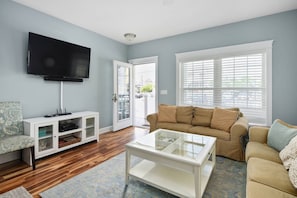 A living room with a TV, white entertainment unit, beige sofa, and a glass coffee table.